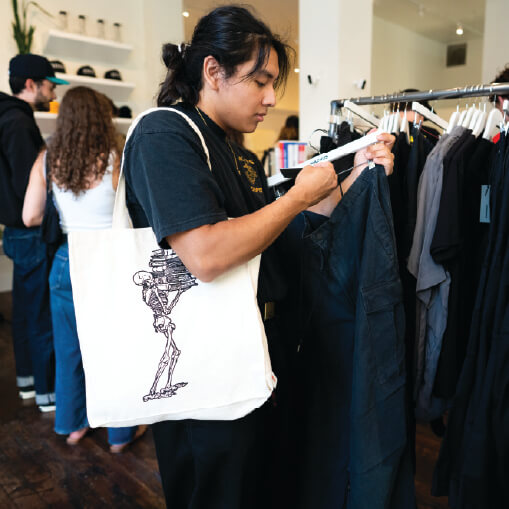 Shopper with tote bag looks through clothing racks and is looking at a pair of pants